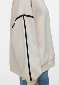 Lys beige genser med løs passform, med svarte kanter langs ermene og ribbestrikkede mansjetter. Mykt stoff med glatt tekstur.