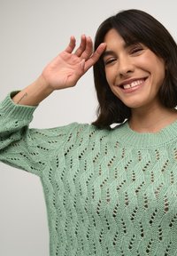 Mint green knitted sweater with a wave pattern, featuring openwork details and a wide crew neckline. Soft texture and relaxed fit.