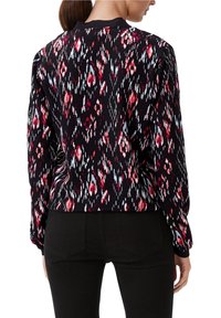 Camiseta de manga larga ajustada con una base negra y un patrón geométrico en rojo y blanco. Tejido suave con un escote acanalado en la parte delantera y trasera.