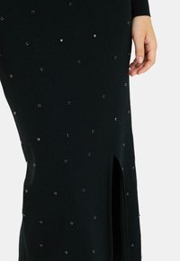 Vestido de punto negro con canalé que presenta una abertura alta en el muslo y adornos dispersos de rhinestones a lo largo del tejido.