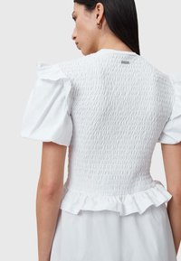 Witte blouse met pofmouwen, gerimpelde textuur op de rug en een gerafelde zoom. Gemaakt van lichtgewicht stof.