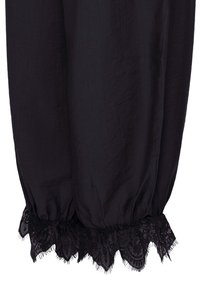 Jambes de pantalon en tissu noir avec ourlets élastiques et bordure en dentelle noire complexe aux poignets sur fond blanc.