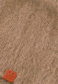 Brązowy filc z miękką teksturą, z małą prostokątną brązową skórzaną metką tłoczoną z napisem "Bickley + Mitchell".