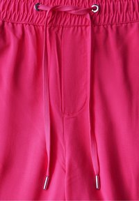 Rosa tygbyxor med elastisk midja, som har en snodd med metallspetsar och sidofickor. Slät textur.