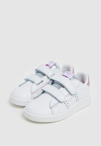Sneakers bianchi con accenti di glitter argento, cinturini in velcro, dettagli rosa e motivi a stella sui lati. Texture in pelle liscia.