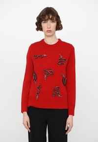 Red knitted sweater featuring intricate snake designs in black and silver, round neckline, and ribbed cuffs and hem.