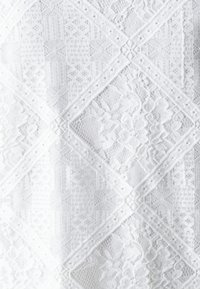 Tissu en dentelle blanche présentant des motifs en diamant complexes, des accents floraux et des détails texturés. Apparence légère et délicate.
