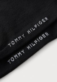 Svarta strumpor i mjukt tyg, med vit text "TOMMY HILFIGER" som är tydligt synlig nära skaftet, med en slät yta.
