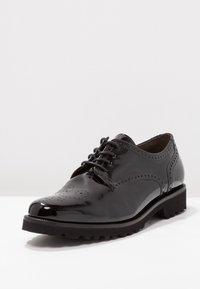 Czarny lakierowany but z okrągłym noskiem, sznurowany, z detalami w stylu brogue oraz grubą, wyjątkowo teksturowaną podeszwą.