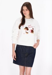 Fehér pulóver barna kutya mintával, rózsaszín kiemelésekkel és a "Happy Puppy" felirattal. Sötét farmer szoknyával párosítva.