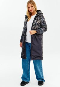 Dlouhý černý péřový kabát s květinovým vzorem v horní části, se zipem a kapucí. V kombinaci se světle modrými kalhotami s širokými nohavicemi a černými botami.