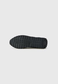Semelle de chaussure en caoutchouc noir avec un motif de crampons profonds comportant des rainures rectangulaires et linéaires, avec un texte de marque centré, isolée sur un fond clair.