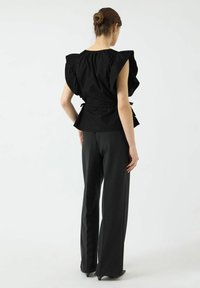 Svart topp med puffede ermer og en innsnevret midje, kombinert med svarte skreddersydde bukser. Jevn tekstur, elegant design og skinnende sko med hæl.