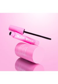 Różowa tubka maskary z czarną szczoteczką aplikacyjną, umieszczona obok różowego cylindrycznego pojemnika, oba z białym napisem i błyszczącym wykończeniem.