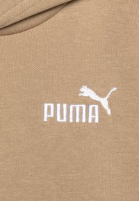 Sudadera beige con una tela suave y texturizada. Presenta un logo bordado en blanco de "PUMA" y la silueta de un puma saltando. Diseño simple, estilo casual.