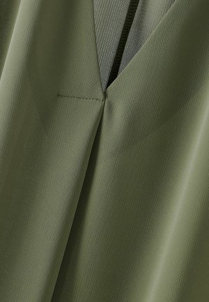Olivengroene stof met een gestructureerde afwerking. Heeft een V-halsontwerp en een zichtbare naad. Het materiaal lijkt lichtgewicht en glad.