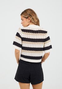 Sweter na krótki rękaw wykonany na drutach z naprzemiennymi czarnymi, beżowymi i białymi paskami, w luźnym, skróconym fasonie z prążkowanym kołnierzem.