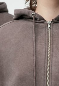 Φούτερ με κουκούλα σε απαλό καφέ ύφασμα, με ολοκληρωμένο φερμουάρ, κορδόνια και απαλή υφή με ορατές λεπτομέρειες ραφής.