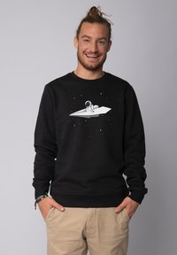 Black sweatshirt featuring a central graphic of an astronaut on a paper plane against a starry background. Ribbed cuffs and hem.