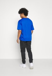 T-shirt bleu royal à manches courtes, en coton, coupe décontractée; associé à un pantalon noir fuselé et des baskets blanches.
