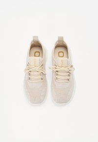 Des chaussures de sport beiges avec un dessus en tricot, dotées de lacets ton sur ton, d'une languette et d'une semelle en caoutchouc blanc. Logo de la marque sur la languette.