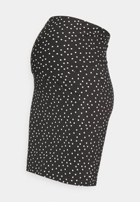 Saia de maternidade preta com bolinhas brancas, tecido liso, design ajustado, até ao joelho e cintura elástica acima da barriga.