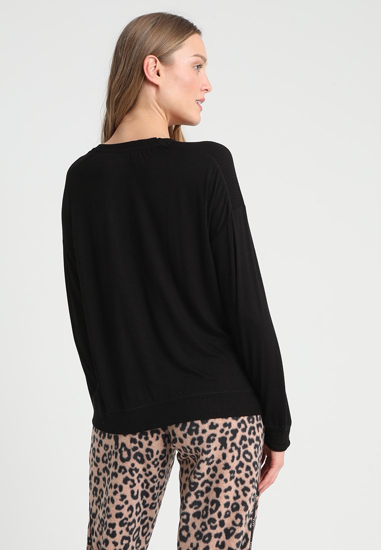 Czarny sweter z dzianiny o luźnym kroju, z prążkowanymi detalami na ramionach i okrągłym dołem. Połączony z spodniami w panterkę.