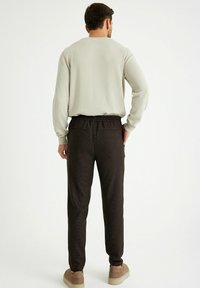 Heren lichtgrijze long-sleeve shirt met een relaxte pasvorm, gecombineerd met zwarte joggingbroek met patroon, voorzien van een elastische tailleband en twee achterzakken.