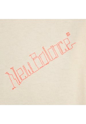 Beige stof bevat de tekst "New Balance" geborduurd in roze draad, met een eenvoudig, blokletterontwerp.
