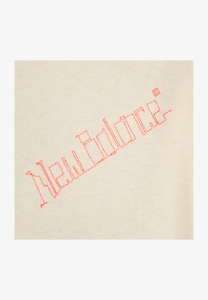 Beige stof har teksten "New Balance" broderet med pink tråd i et simpelt blokbogstavsdesign.