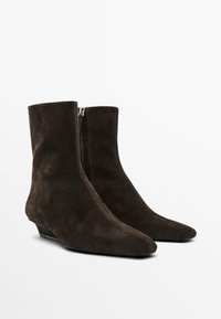 Bottines en daim marron avec un bout pointu, texture lisse, fermeture éclair à l'avant et talon compensé bas.