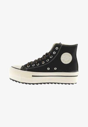 Sneaker alta nera in tela con punta in gomma bianca e suola platform spessa. Presenta occhielli rotondi e una toppa con logo circolare sul lato.