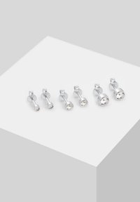 Šest pari srebrnih naušnica s prozirnim okruglim dragim kamenjem, posloženih po rastućem redoslijedu veličine na bijeloj nagnutoj površini.