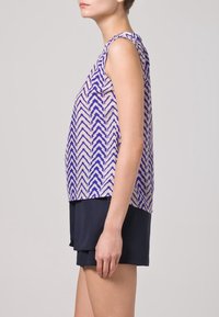 Hihaton toppi kevyestä kankaasta, jossa on geometrinen purppuranvärinen herringbone-kuvio vaalean kermaisen taustan päällä, yhdistetty tummiin shortseihin.