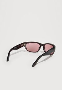 Γυαλιά ηλίου με μαύρο πλαίσιο από πλαστικό και ροζ φιμέ φακούς, ανοιχτά τοποθετημένα πάνω σε λευκή επιφάνεια, σε λήψη από πίσω-δεξιά γωνία.