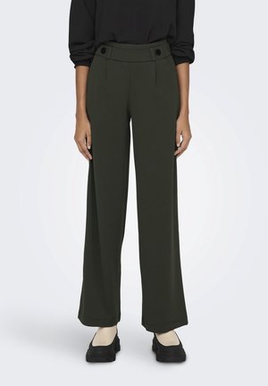 Pantalons larges verts à taille haute, avec des accents de boutons à la taille et une texture lisse. Associés à des chaussures à plateforme noires.
