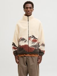 Jachetă din fleece de culoare crem, cu guler înalt, fermoar negru și un model montan în nuanțe de roșu, gri și alb. Croială texturată, supradimensionată.