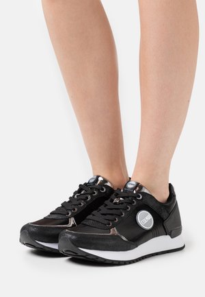 Mustat urheilukengät, joissa on tekstuuria omaava nahka ja verkkopäällinen, metalliset yksityiskohdat, valkoinen pohja ja logo sivulla. Kengissä on nauhoilla suljettavan suunnittelu.