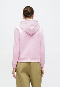 Ροζ φούτερ με  κουκούλα και κορδόνι, ριμπ μανσέτες και στρίφωμα, συνδυασμένο με παντελόνι ανοιχτού ελαιδί χρώματος. Μαλακό ύφασμα και μίνιμαλ σχεδιασμός.