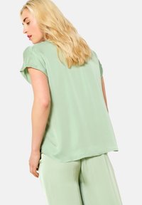 Light green satin top with short sleeves, featuring a rounded hem and smooth texture, paired with matching light green pants.
