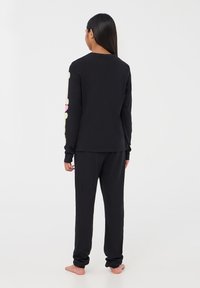 Czarny zestaw odzieży domowej z długim rękawem i spodniami. Bluzka ma duże, abstrakcyjne kolorowe kształty na rękawach. Miękki, swobodny materiał.