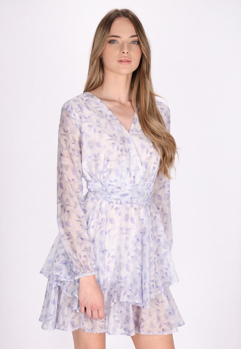 Leichtes, durchscheinendes Kleid mit lilafarbenem Blumenmuster, V-Ausschnitt, langen Ärmeln und mehrlagigem Rüschensaum. Der strukturierte Stoff unterstreicht das Design.