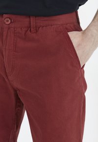Pantalones de algodón color burdeos con parte delantera plana, bolsillos laterales y cierre de botón. Presentan una textura suave y un diseño de pierna recta.