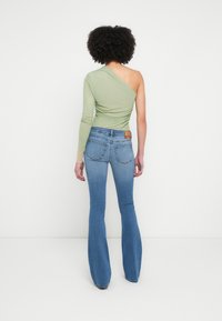 Asümmeetriline roheline pika varrukaga topp, mis on sobitatud helesiniste kellukakujuliste teksadega. Topil on keha järgnev lõige ja ühel küljel voltimisega detail.