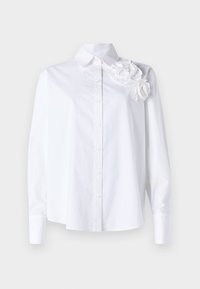 Camicia bianca a maniche lunghe in cotone. Presenta un colletto a banda larga e tre fiori in tessuto testurizzato sulla spalla sinistra.