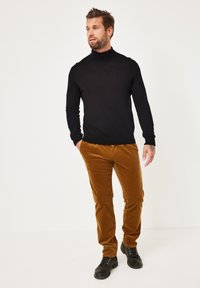 Schwarzer Rollkragenpullover kombiniert mit braunen Cordhosen und schwarzen Schnürstiefeln. Der Pullover ist figurbetont und die Hose hat ein strukturiertes Muster.
