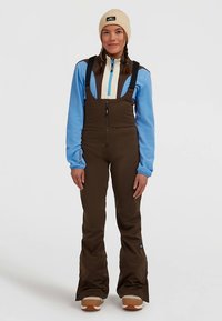 Rudos vandeniui atsparios slidinėjimo kelnės su bretelėmis, mėlynas ilgas rankovės marškinėlis su užtrauktuku, kreminės spalvos megzta kepurė, faktūrinė medžiaga, praplatintos kelnės, kontrastingos detalės.