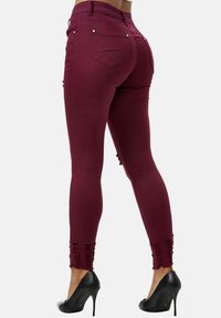 Vaqueros skinny burdeos con textura suave, cintura alta y detalles deshilachados en el dobladillo. Combinados con zapatos de tacón negro.
