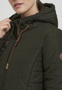 Quilted dark green puffer jacket with a drawstring hood, brown accents, and a front zipper. Features a logo patch on the sleeve.