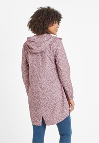 Light purple rain jacket with a repeating abstract pattern, featuring a hood, elastic cuffs, and a longer back, paired with blue jeans.